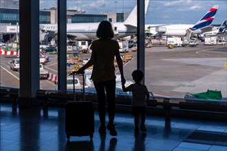 Silhouette of mother and son with luggage standing near the window in the airport