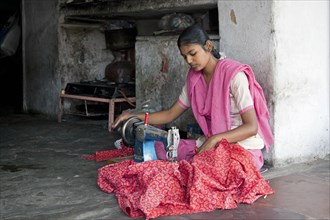 Indian girl sitting cross-legged making clothes with old sewing machine at tailoring store in Jaipur