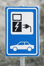 Electric car charging station sign at car park in the snow in winter