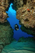 Diver swimming through cave tunnel of coral rock in coral reef