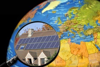 Photovoltaic solar panels on roof of house seen through magnifying glass held against illuminated terrestrial globe