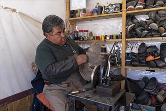 Old-fashioned Bolivian shoemaker with old sewing machine mending shoes in market stall in the city Uyuni