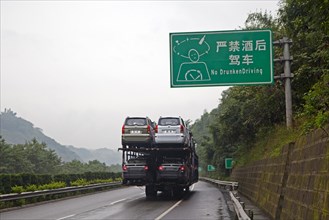 Typical Chinese side-by-side double-decker car transporter and No Drunken Driving roadsign along highway