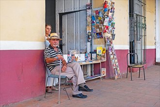 Proud Cuban senior bookseller posing in front of his little bookshop