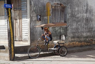 Street scene showing man on three-wheeled bicycle taxi waiting for tourists in the city Baracoa
