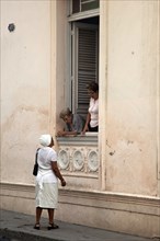 Elderly Cuban women in window talking to black Afro-Cuban woman in Santiago de Cuba