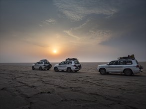 Tourists in off-road vehicles driving on salt desert at sunrise
