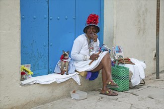Licensed street model posing for tourists as colourful Cuban woman smoking huge Havana cigar with dressed cat in the streets of Old Havana