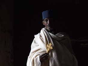 Priest with cross in dark light