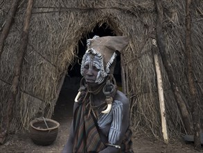 Woman from the Mursi tribe with headdress and face painting in front of her hut
