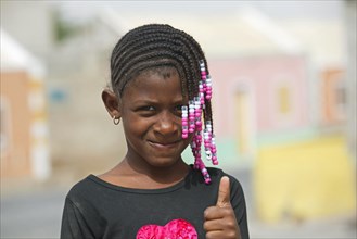 Creole girl with braided hair decorated with colourful beads showing thumbs up on the island Boa Vista