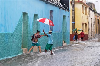 Cubans with umbrellas walking in flooded street during torrential rain in the city Santiago de Cuba on the island Cuba
