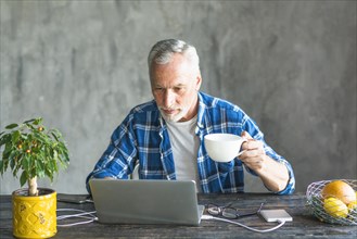 Close up senior man holding coffee cup using laptop charged with power bank