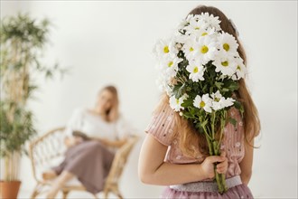 Little girl holding bouquet spring flowers as surprise her mother