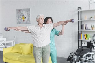 Nurse helping her senior female patient exercising with dumbbells