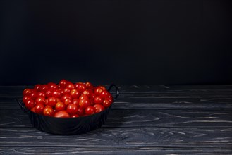 Cocktail tomatoes in black pot on wood