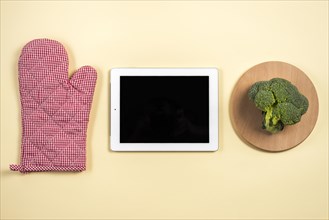 Mitt oven glove digital tablet broccoli wooden tray against beige background