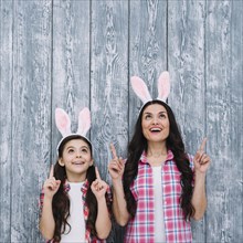Excited mother daughter with bunny ears pointing finger upward against wooden backdrop