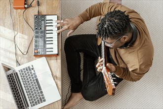 Top view male musician home playing guitar mixing with laptop