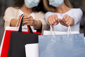 Two defocused women with medical masks holding shopping bags with sale items