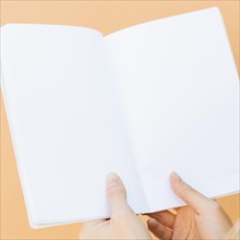 Close up hands holding blank white book against colored backdrop