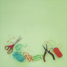 Scissor plier wool beads orange yarn spool green background