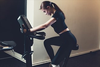 Side view young woman riding exercise bike