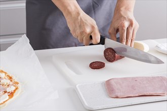 Close up woman s hand cutting salami slices with sharp knife chopping board