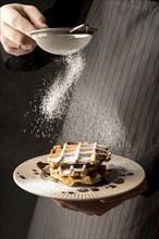 Front view man coating waffles with powdered sugar