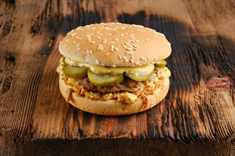 Beef burger with pickled cucumber and onion crumbs on wooden background