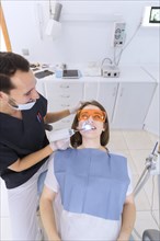 Happy male dentist checking patient s teeth with dental uv light equipment clinic