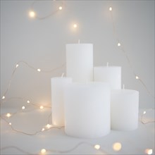 Illuminated fairy lights around white candles grey background