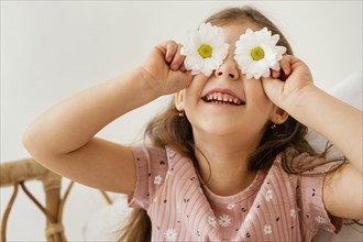 Smiley little girl playing with spring flowers covering her eyes