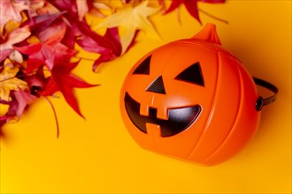 A Halloween pumpkin on red autumn leaves and a yellow background