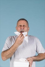 Senior man holding tissue paper about sneeze blue background