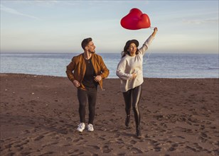 Happy couple running sea shore with heart balloons