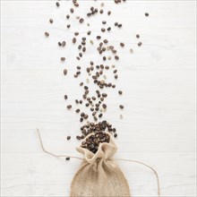 Raw roasted coffee beans falling from small sack desk