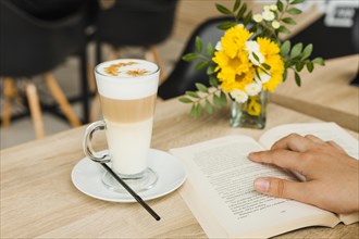 Person reading book near coffee cup desk caf