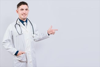 Handsome doctor pointing a promotion with finger. Latin doctor pointing at advertising space isolated. Happy doctor pointing right with finger