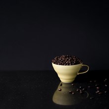 Ceramic cup filled with roasted coffee beans black background