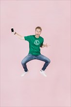 Excited man with smartphone jumping pink backdrop
