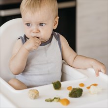 Cute baby boy highchair eating vegetables
