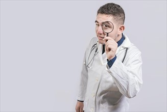 Doctor holding magnifying glass and looking at camera on isolated background. Doctor with magnifying glass looking at the camera