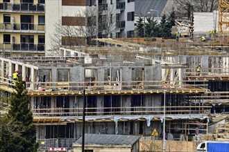 Construction workers install formwork and iron rebars or reinforcing bar for reinforced concrete partitions at the construction site of a large residential building on sunny spring day. Modern houses