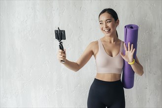 Smiley woman vlogging with her phone while holding fitness mat
