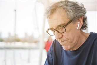 Senior man wearing eyeglasses with white bluetooth earphone his ear