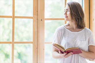 Pretty young woman standing front window holding book