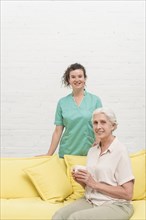 Smiling senior woman sitting sofa holding coffee cup front nurse