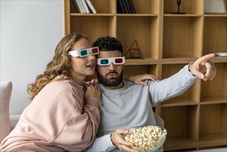 Couple watching movie home with three dimensional glasses eating popcorn