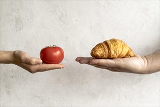 Human hand showing croissant red tomato front concrete background